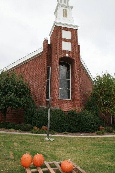 Brick church with a steeple and pumpkins on a wooden pallet in the foreground