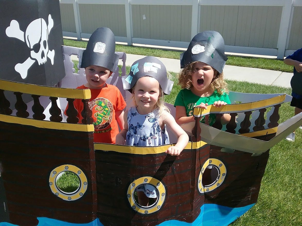 Three children in pirate hats playing in a cardboard pirate ship
