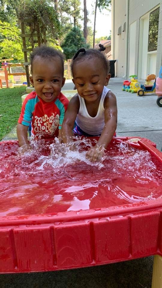 Two children splashing water in a red water table outdoors
