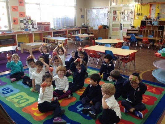 Children sitting on a rug in a classroom, holding apples
