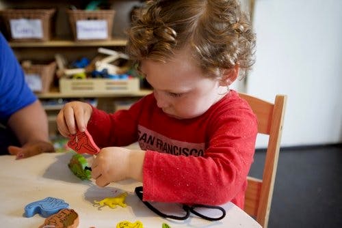 Child in red shirt playing with small toys at a table