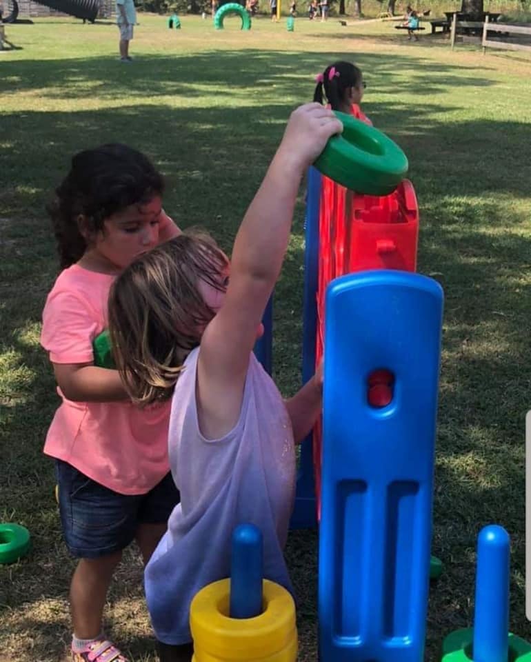 Two children playing with colorful plastic rings and poles outdoors