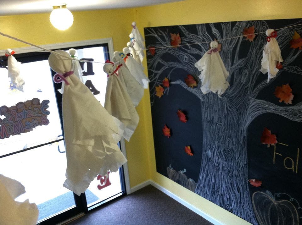 Ghost decorations hanging on a string in a room with a chalk drawing of a tree