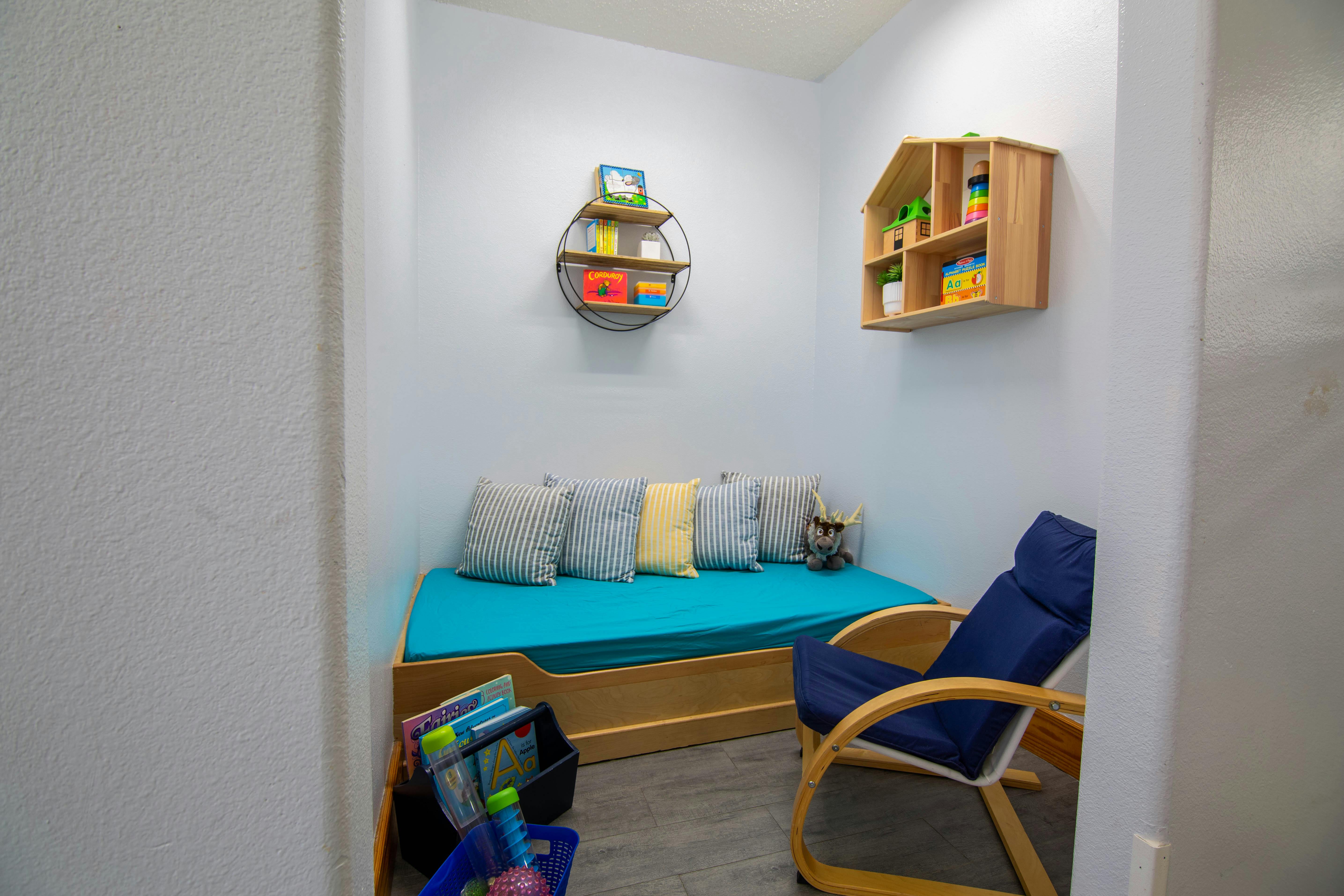 Small room with daybed and blue cushion, shelves with toys and books