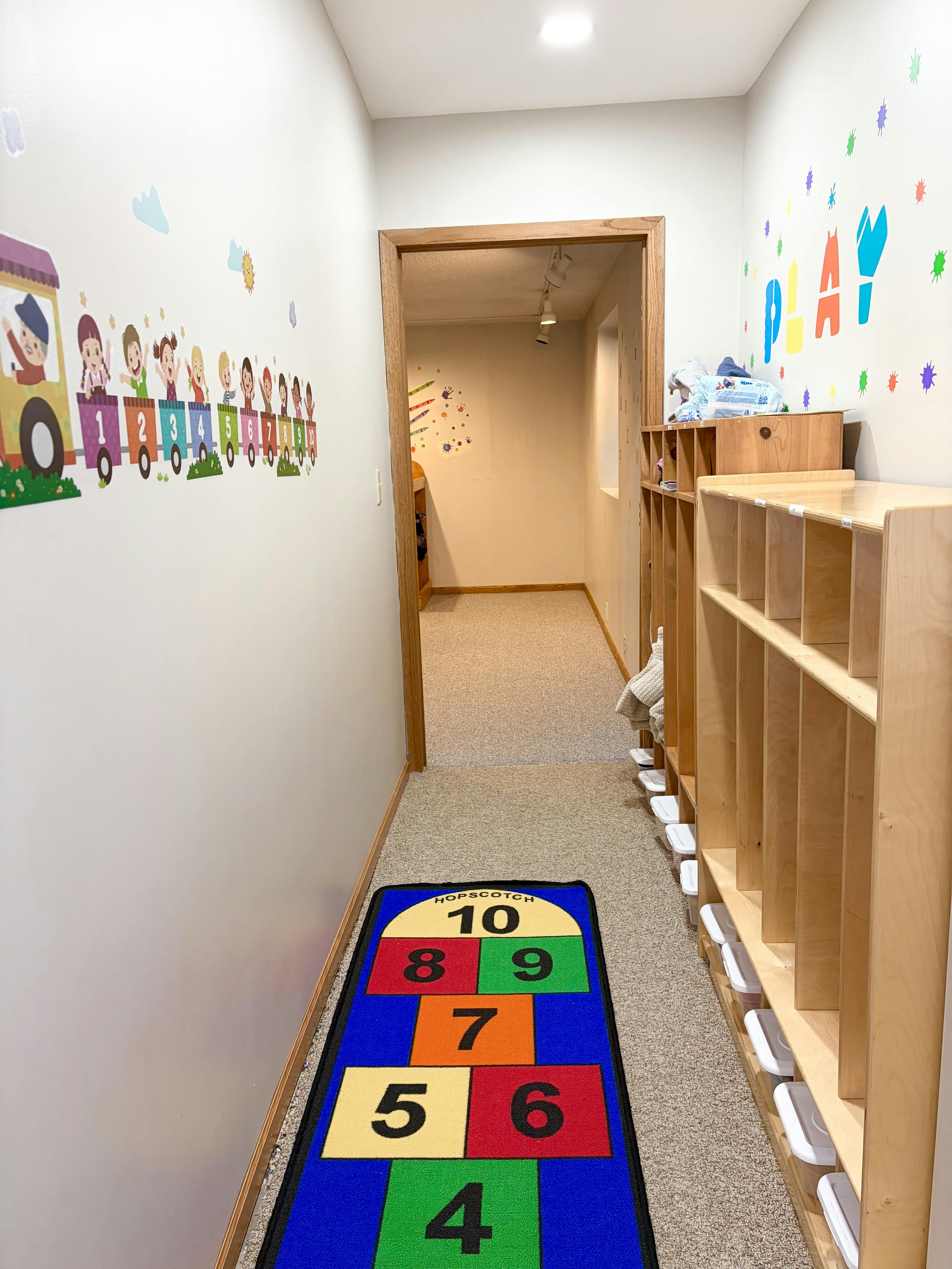 Hallway in a child care facility with a hopscotch rug and cubby storage