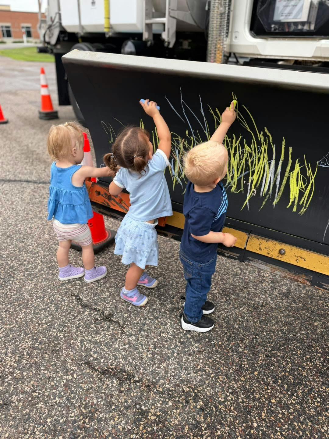 Three children drawing with chalk on the blade of a snowplow