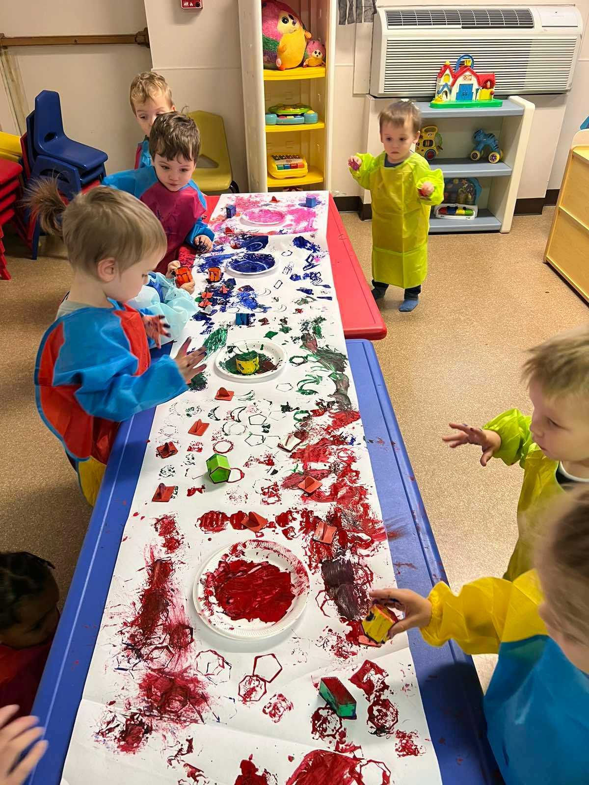 Children painting at a long table in a classroom