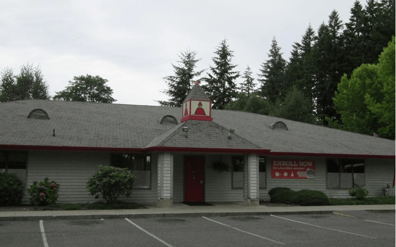 Building with red door and cupola, parking lot in foreground, trees in background