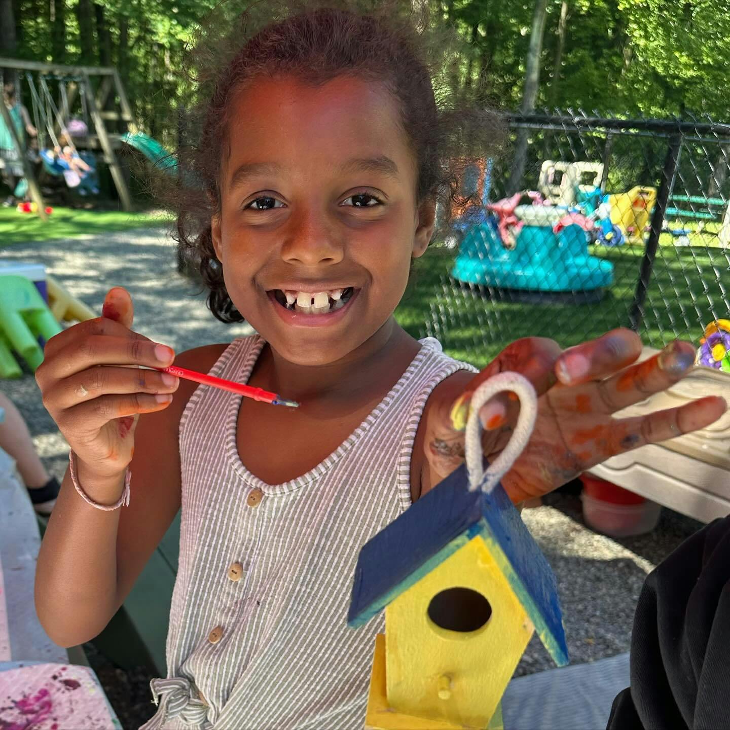 Child holding a paintbrush and a painted birdhouse