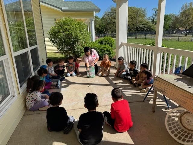 Group of children sitting in a circle on a patio with an adult