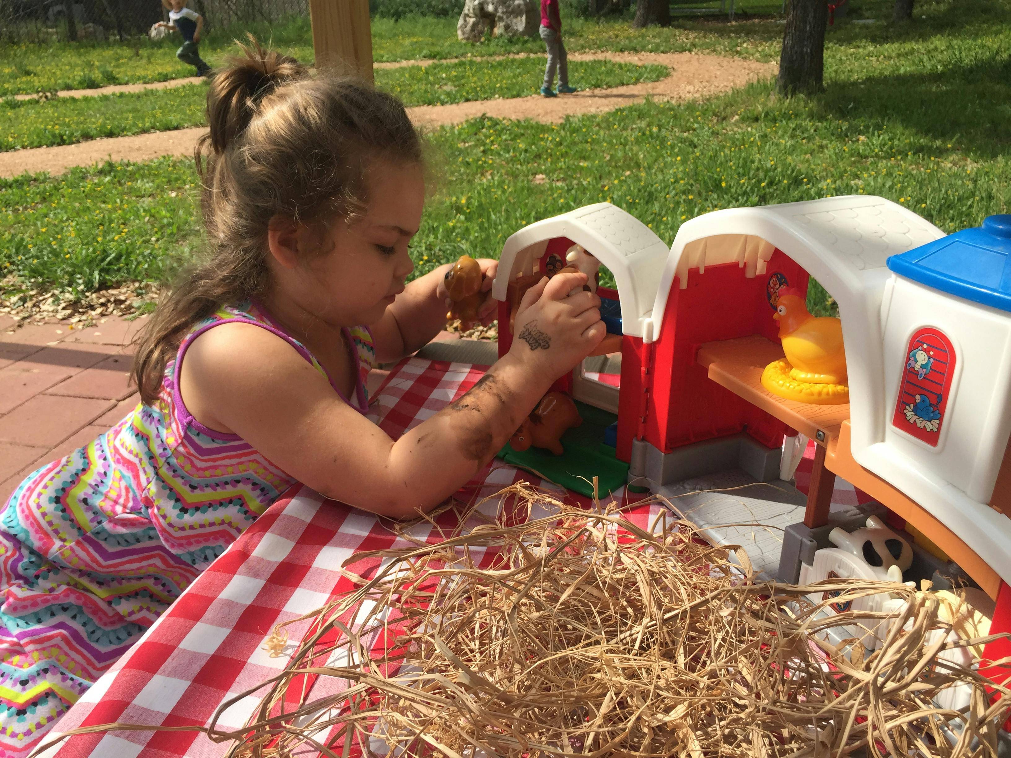 Child playing with a toy barn on a red and white checkered tablecloth