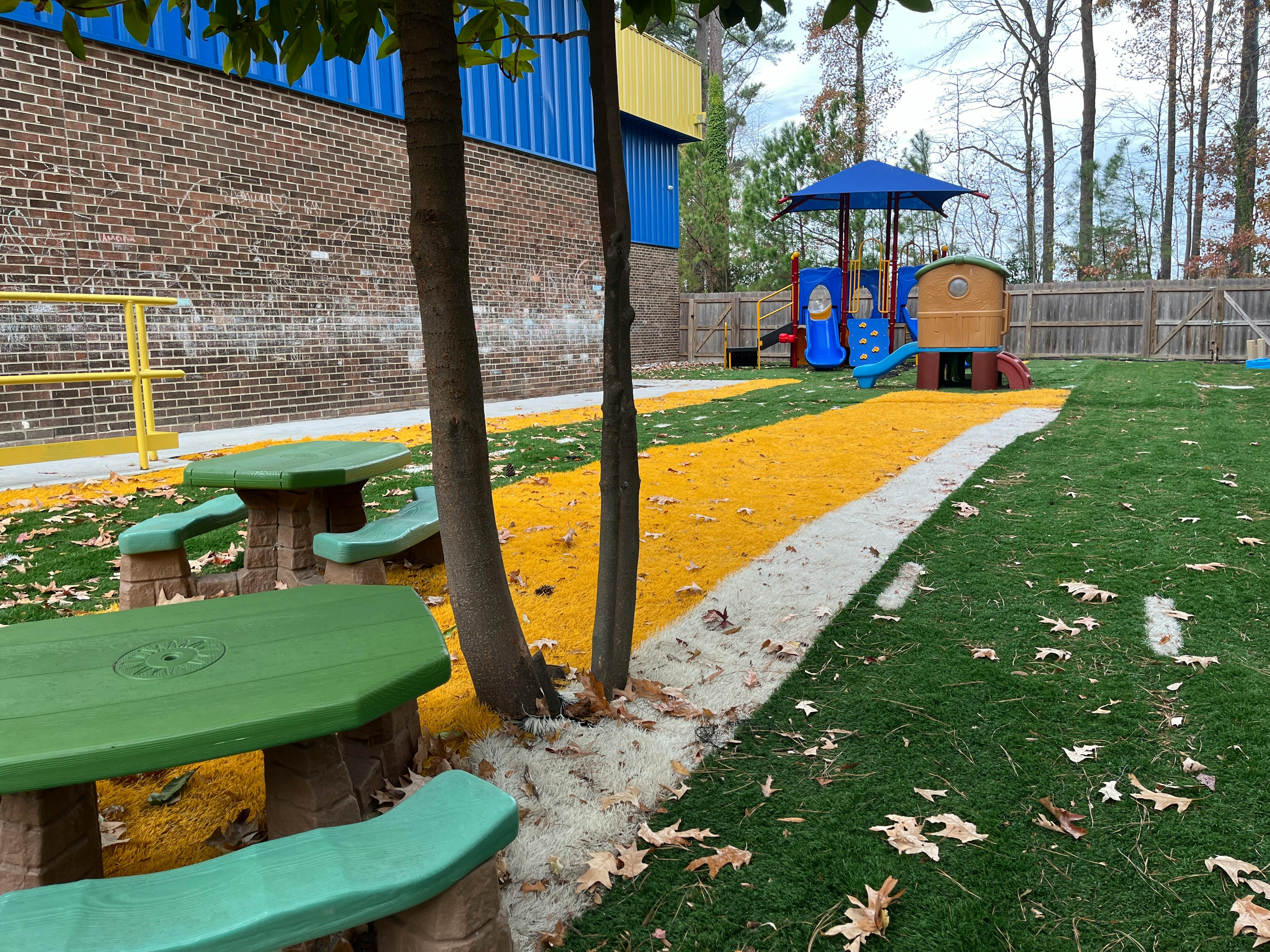 Outdoor playground with green picnic tables, yellow path, and play structure