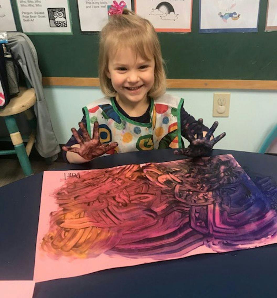 Child with paint on hands and paper with colorful paint