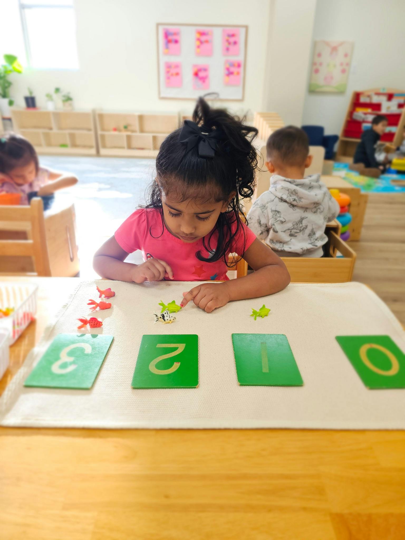 child playing with colorful fish-shaped counters and number cards in a classroom