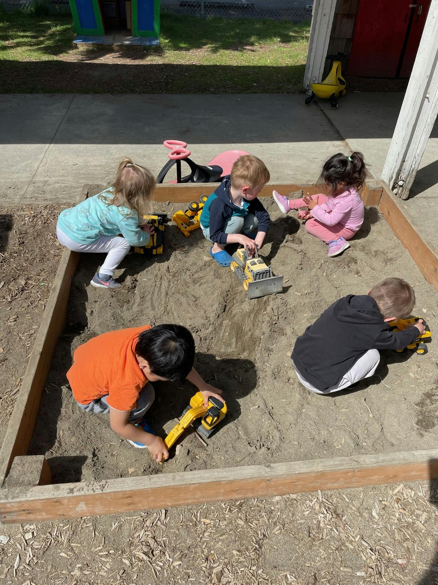 Children playing in a sandbox with toy trucks