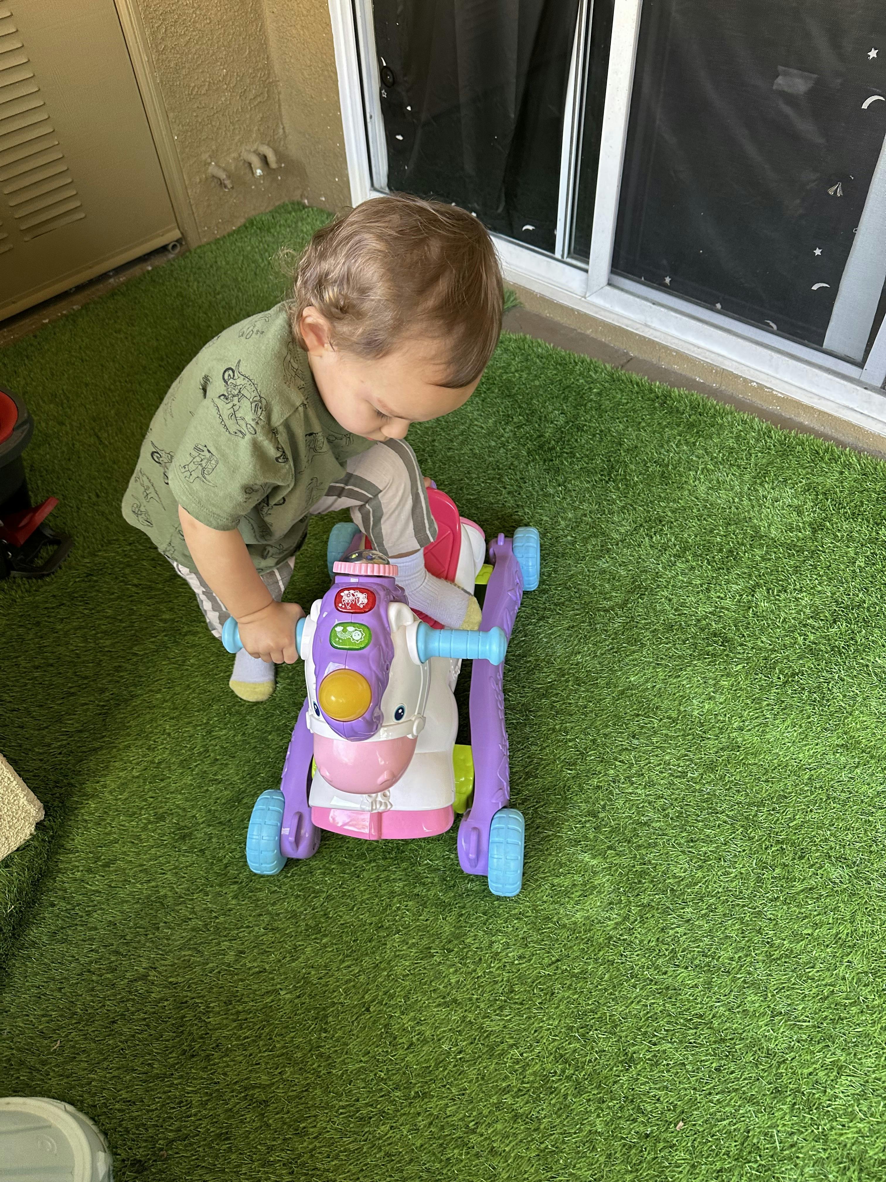 Child kneeling on artificial grass, playing with a colorful toy
