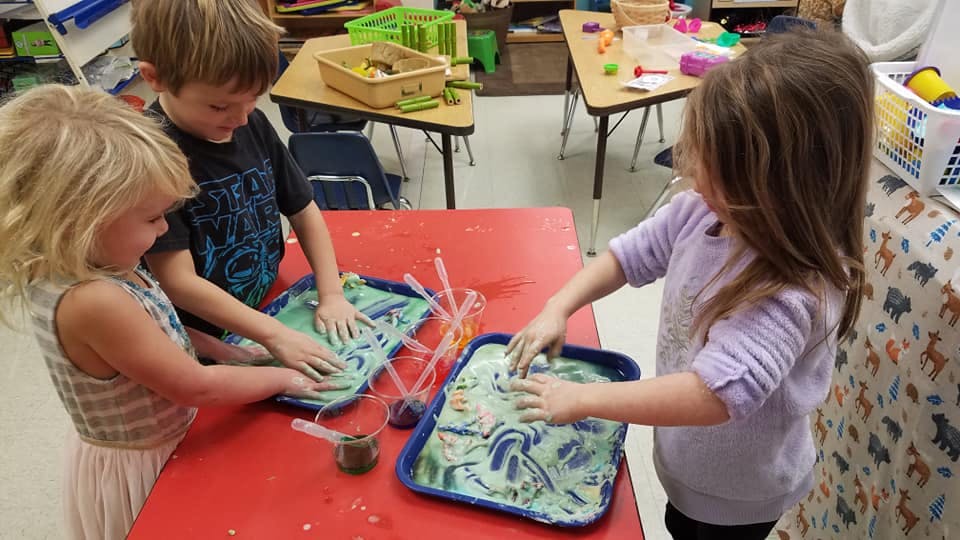Three children playing with sensory bins at a table