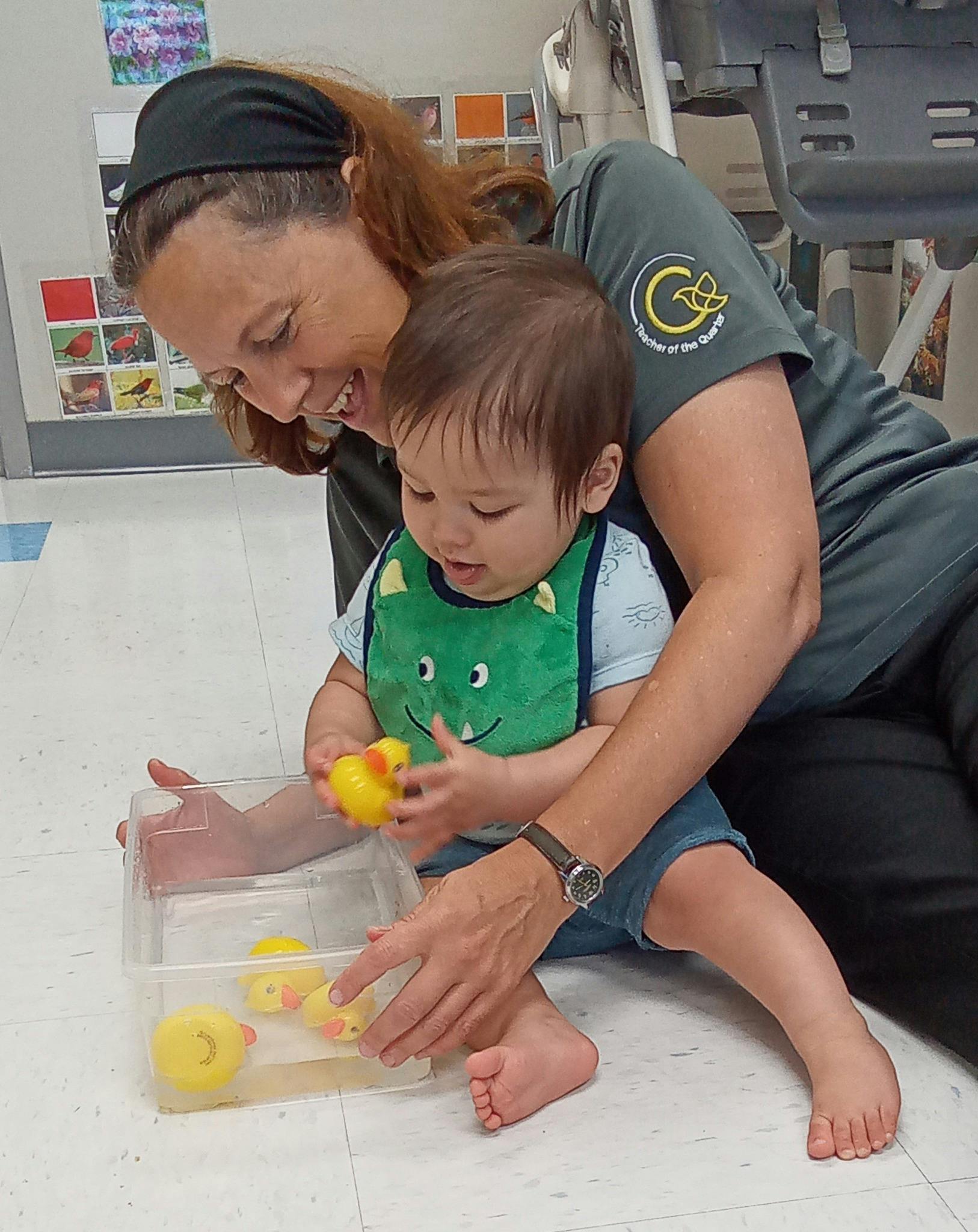Person and child playing with rubber ducks in a clear container