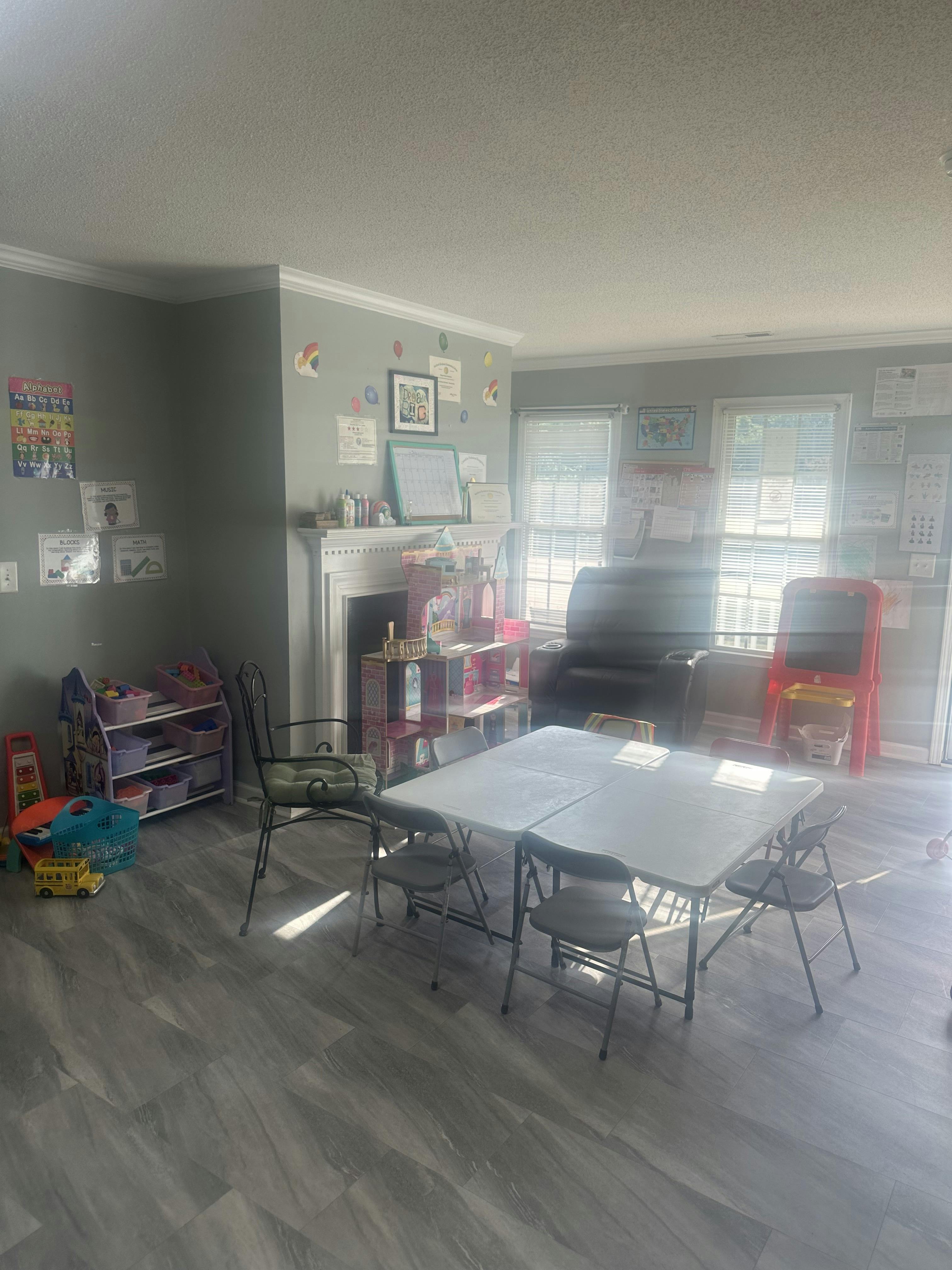 A room with a fireplace, two tables with chairs, and shelves with toys