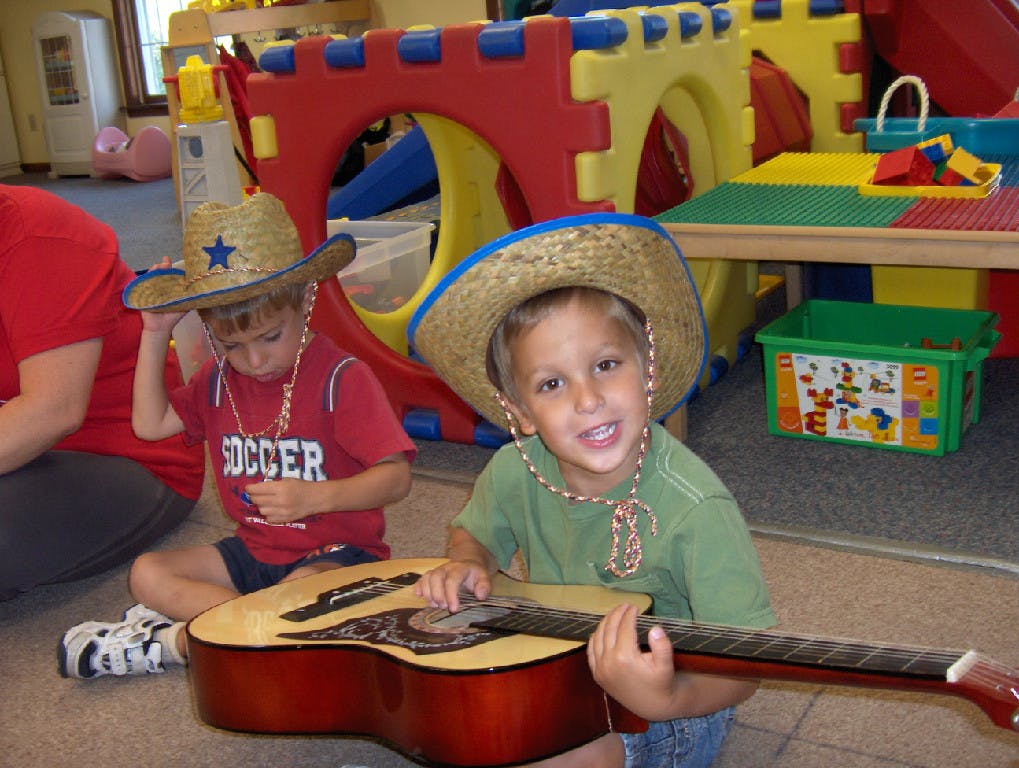 Two children wearing straw hats, one playing a guitar