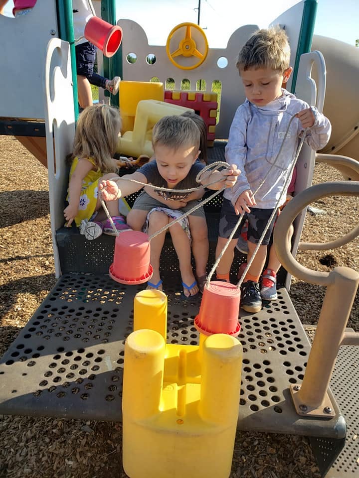 Three children playing with buckets and ropes on a playground structure