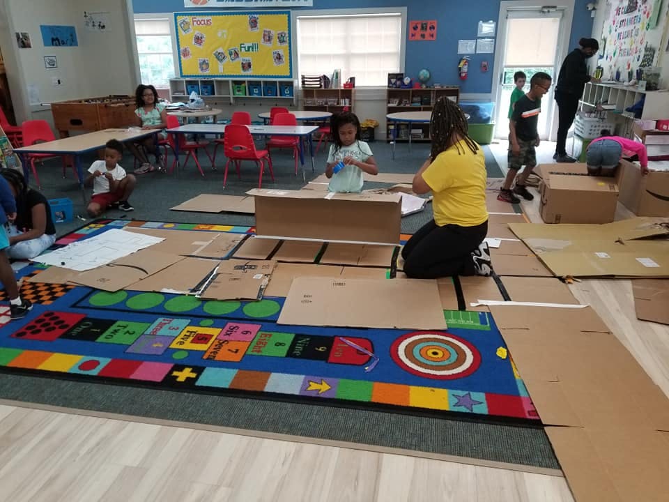 People and children in a classroom with cardboard on the floor