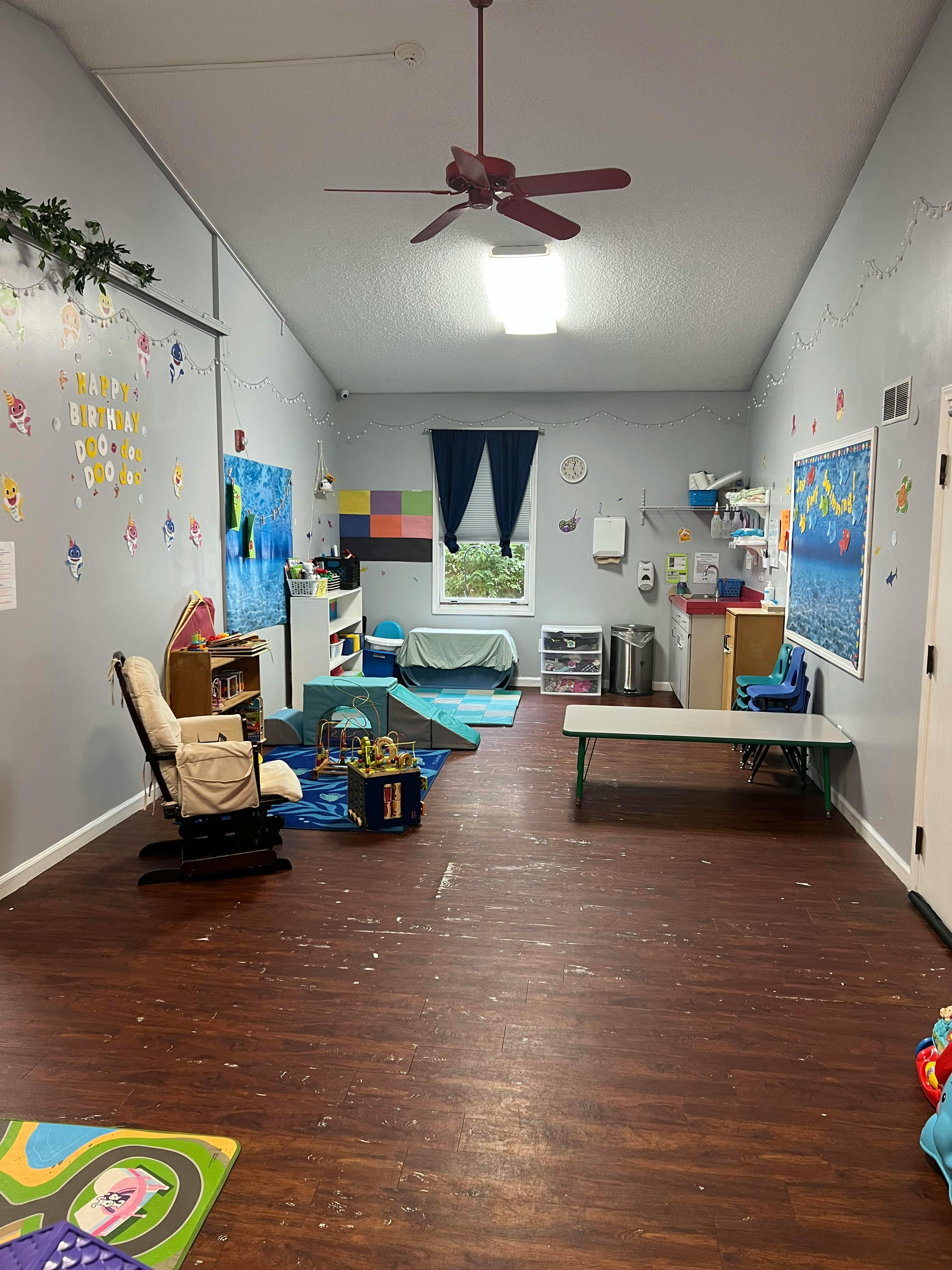 A classroom with a rocking chair, play mats, and a table