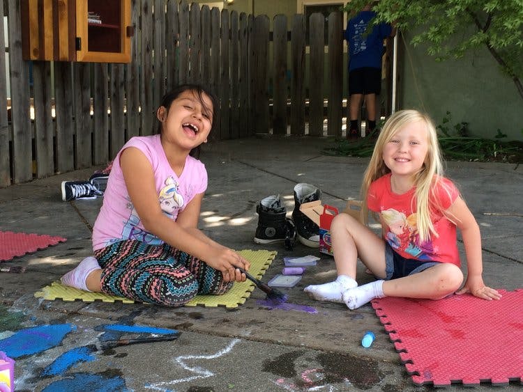 Two children sitting on mats on the ground, one holding a brush