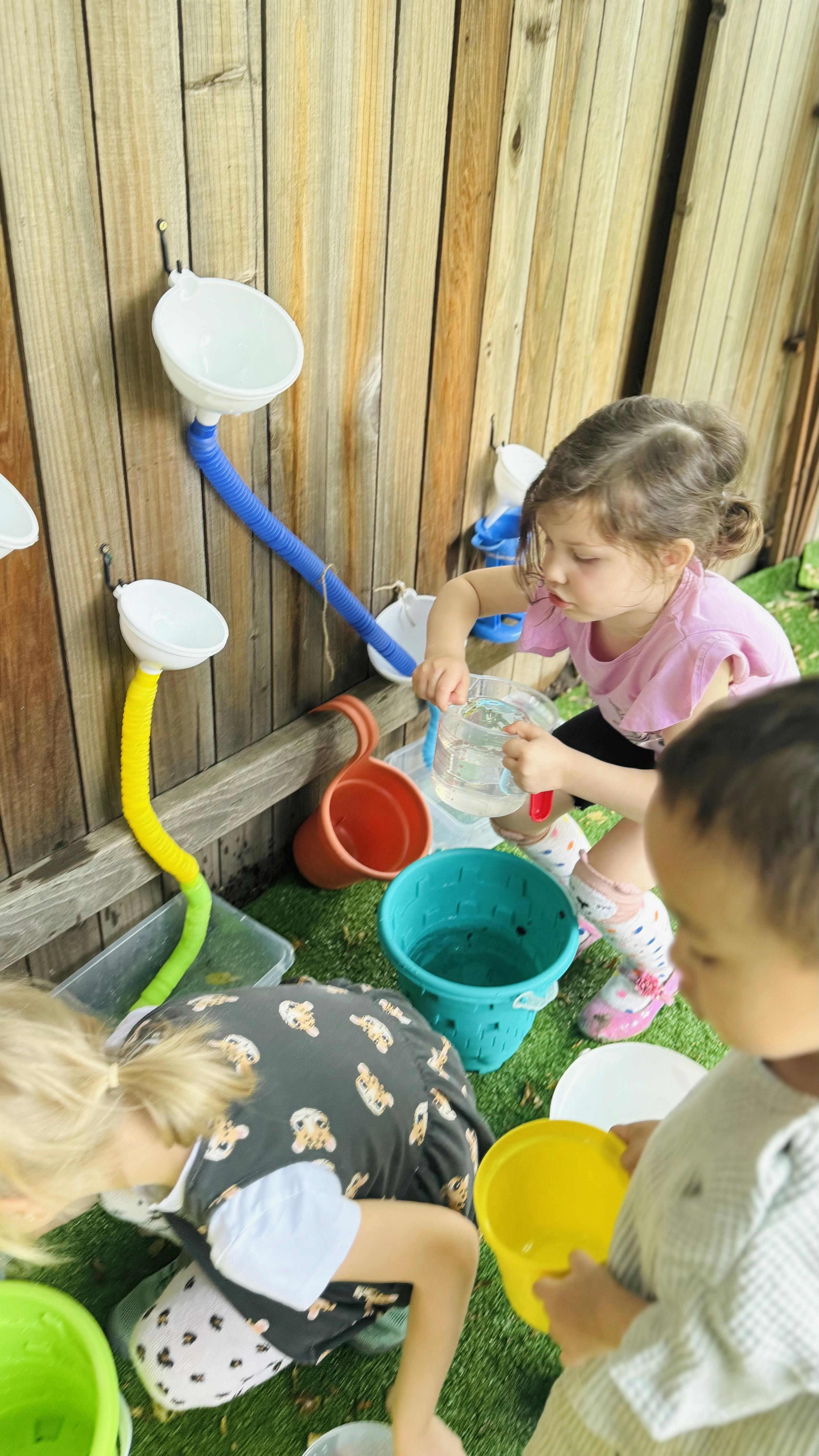 Child pouring water into a funnel attached to a wooden wall