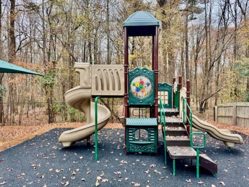 Empty playground with tan and green slides, stairs, and forest in background