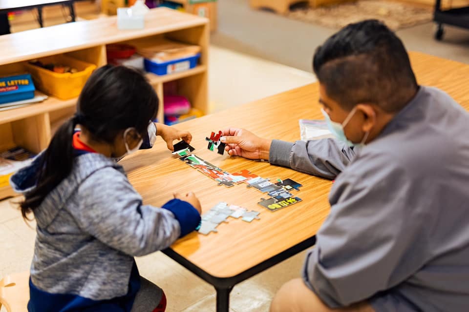 Adult and child wearing masks doing a puzzle at a table