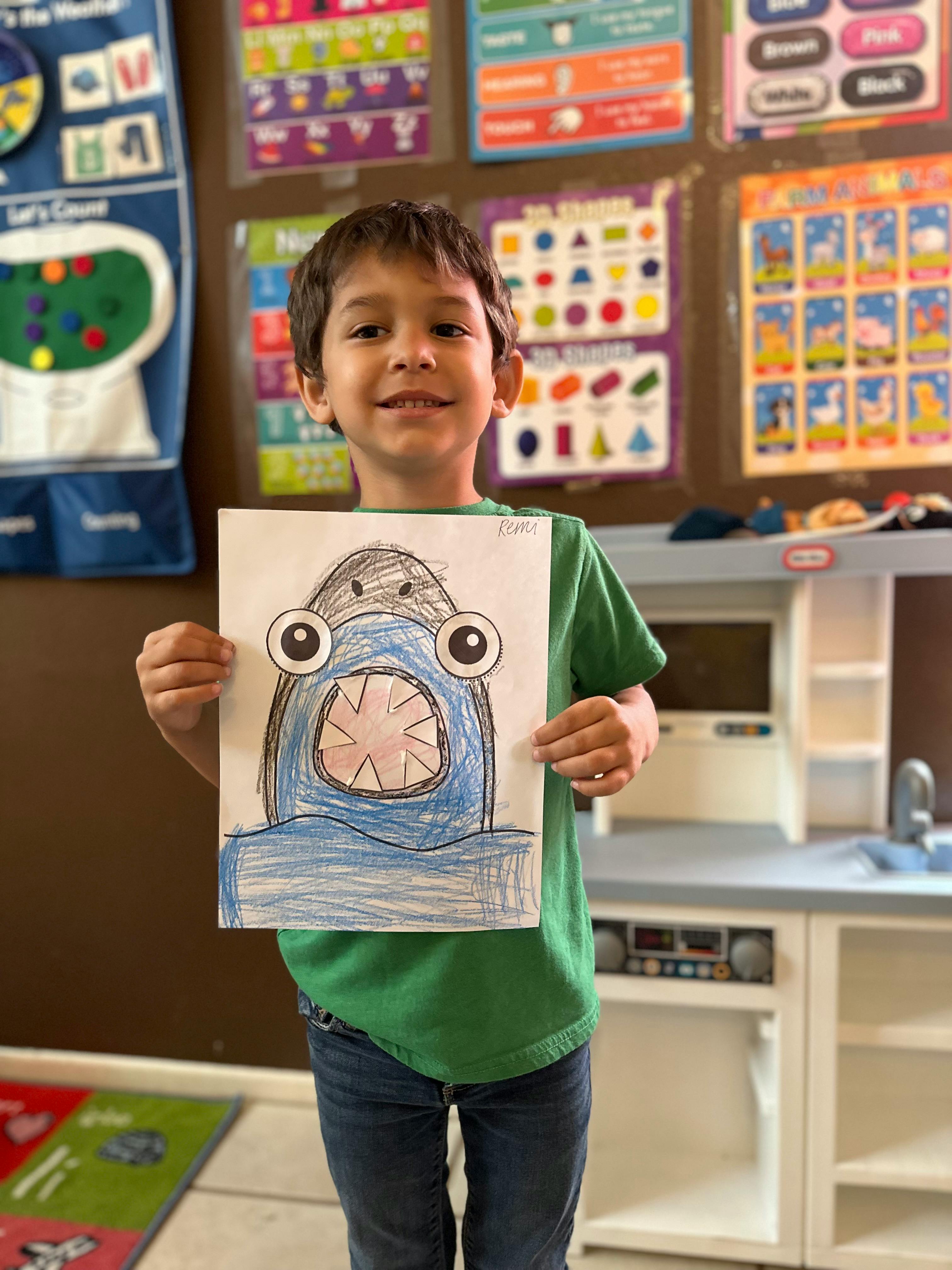 Child holding up a drawing of a blue monster with large eyes and an open mouth