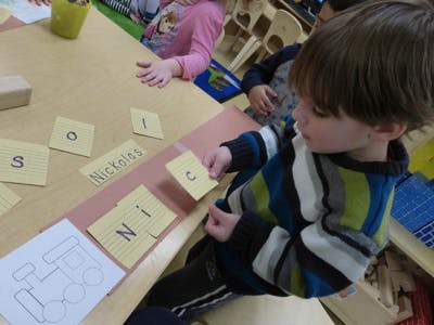Child holding a letter card at a table with other letter cards