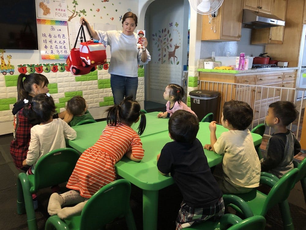 Person holding up a red bag and a doll to a group of children in a classroom