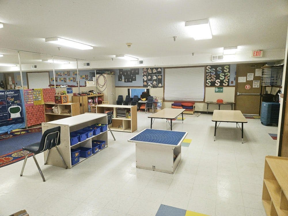 Empty classroom with tables, chairs, and shelves against the walls