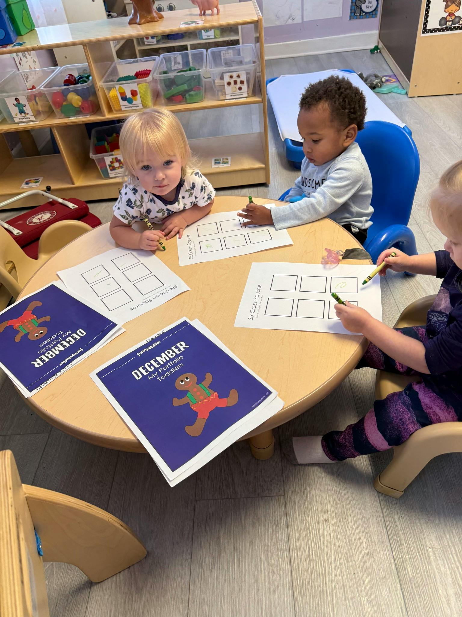 Three children coloring at a small round table in a classroom