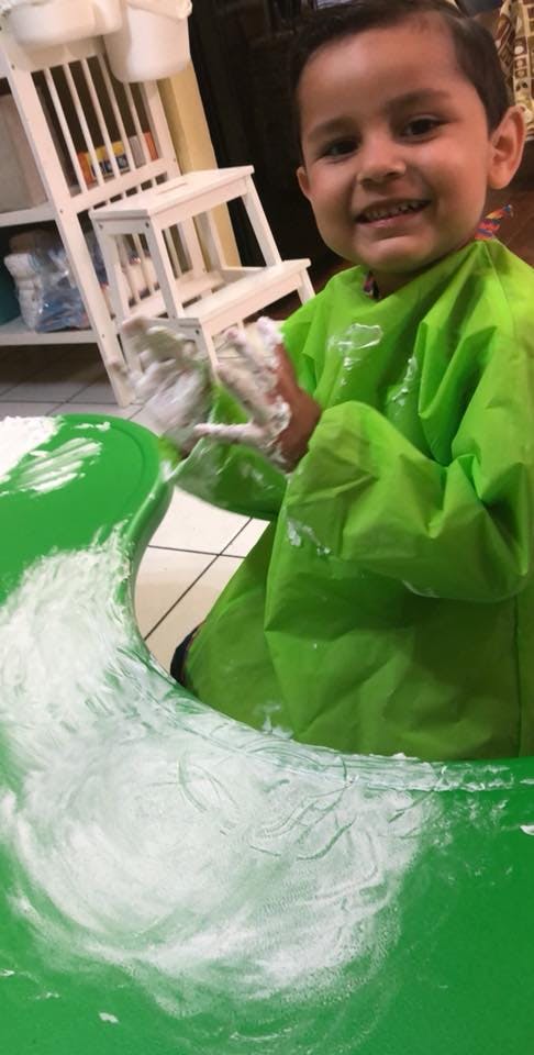 Child in a green smock playing with white powder