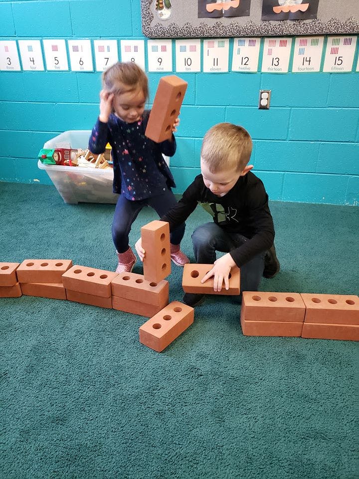 Two children playing with toy bricks on a green carpet