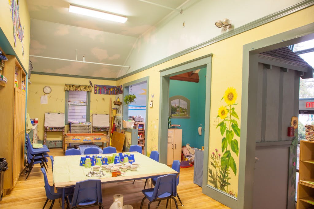 Classroom with a large table and chairs, whiteboards, and a sunflower mural