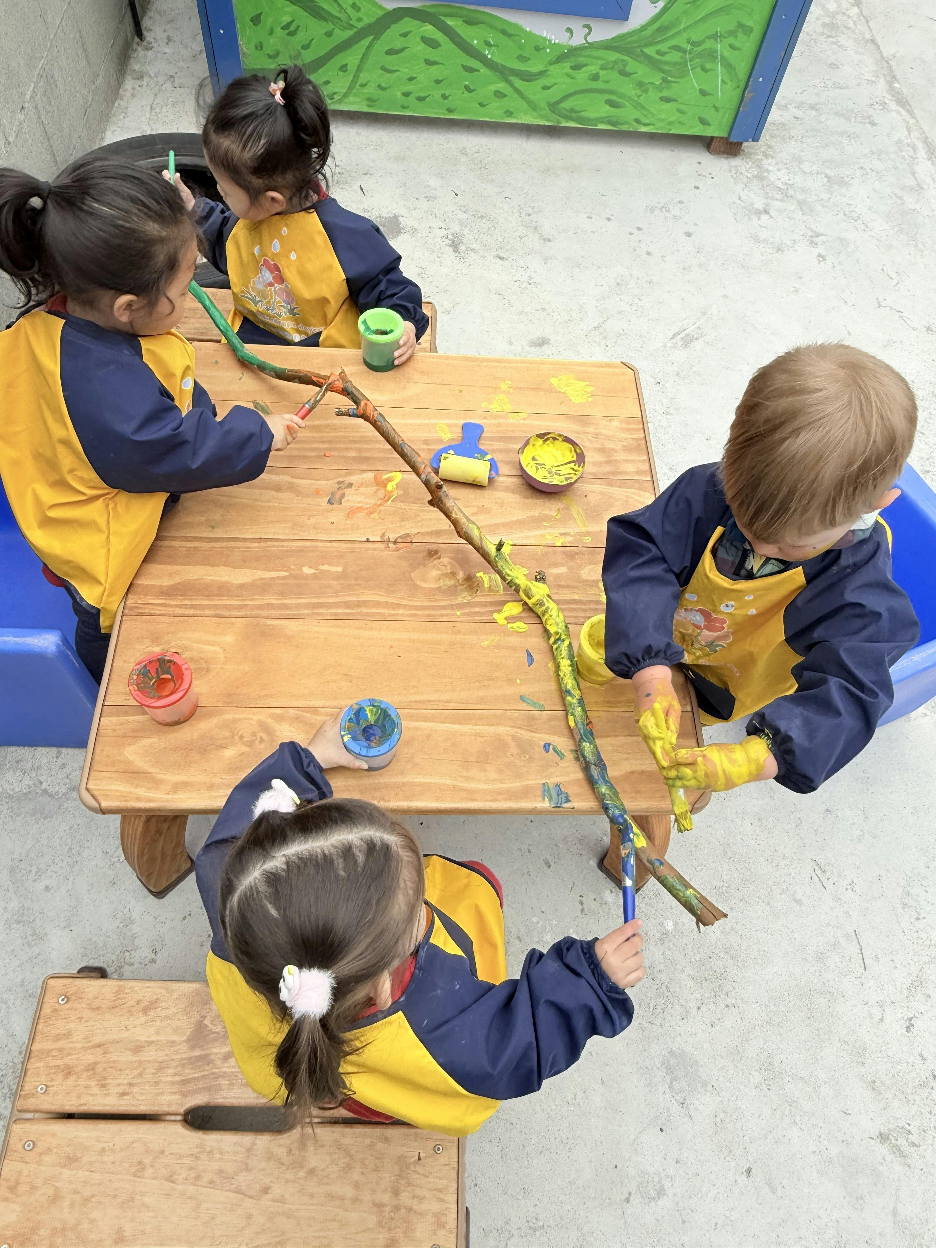 Children painting sticks at a table