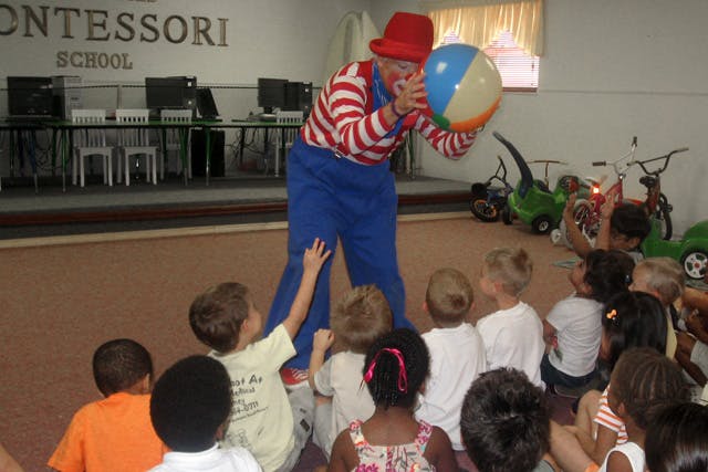 Person dressed as a clown holding a beach ball for a group of children