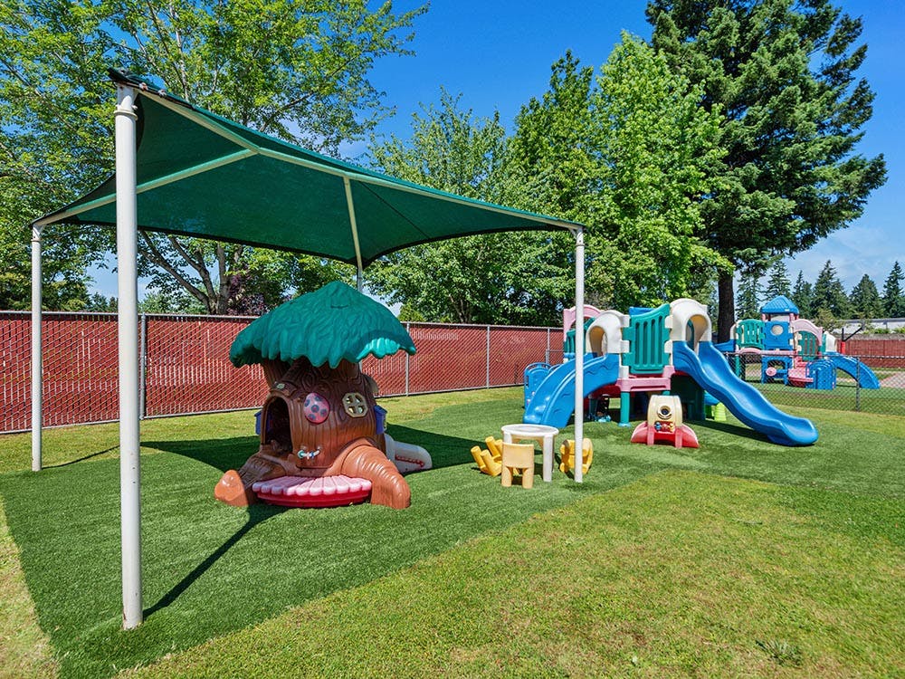Outdoor playground with artificial turf, play structures, and a shade cover
