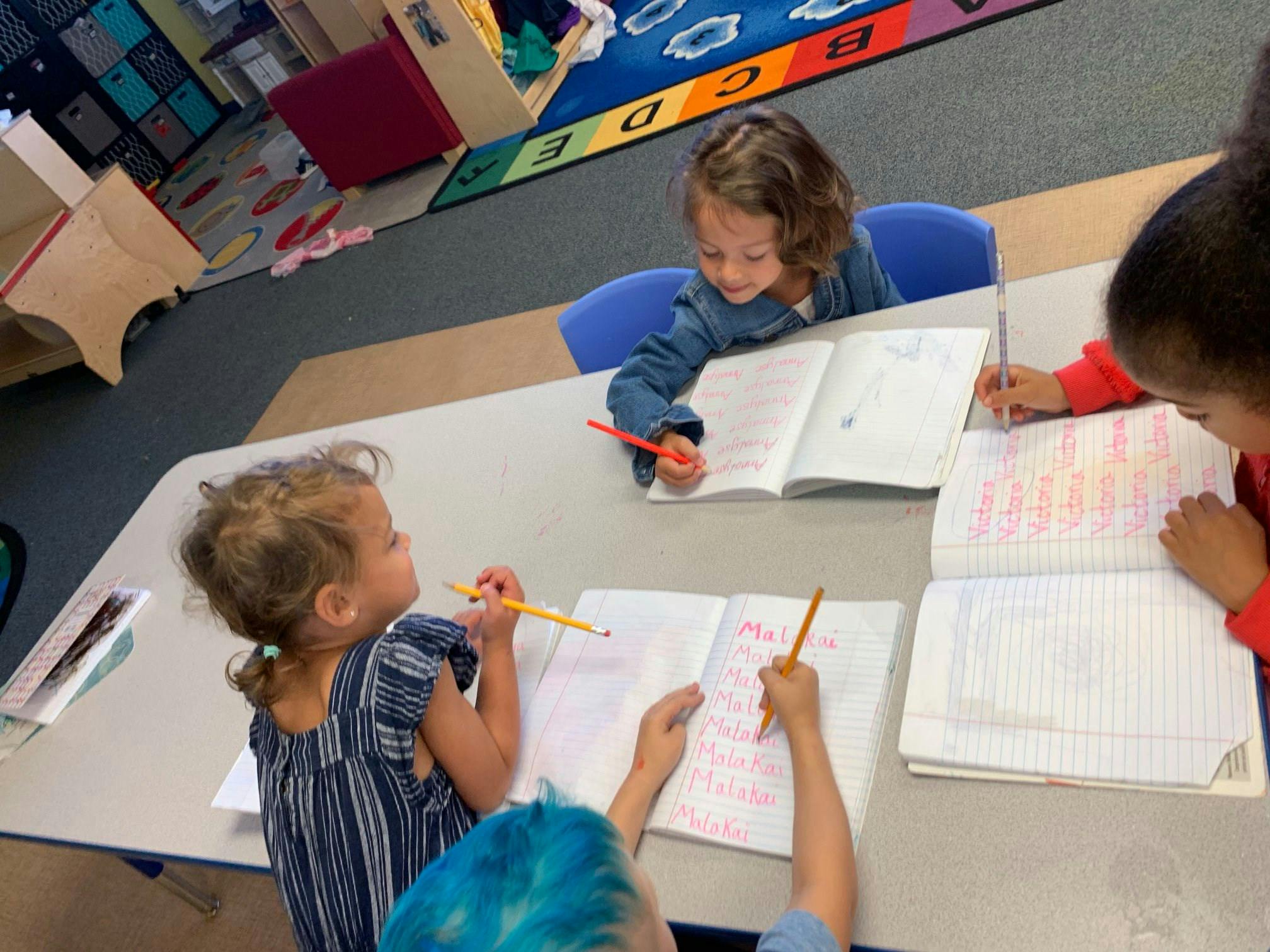 Children writing in notebooks at a table in a classroom