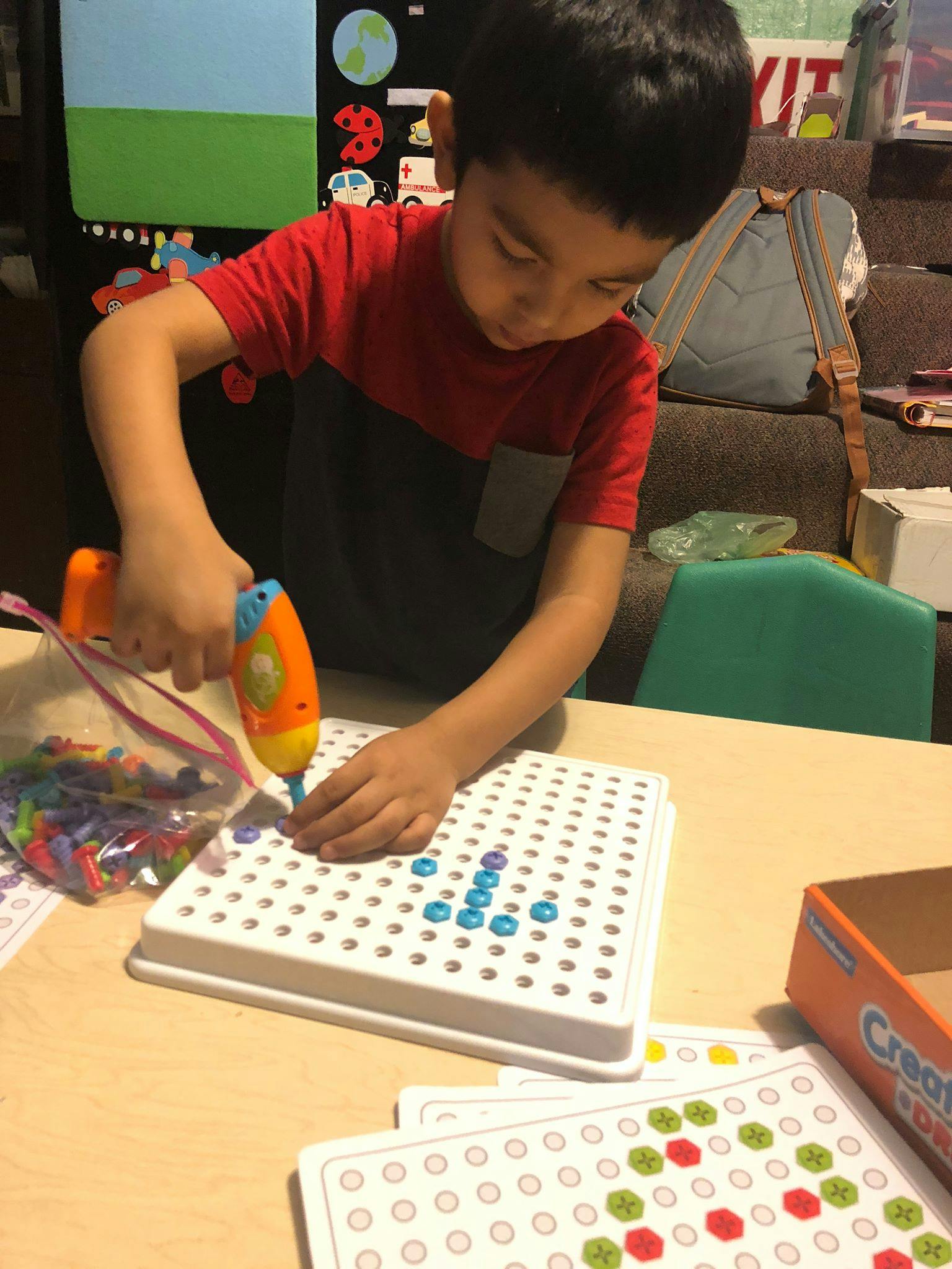 Child using a toy drill to place pegs into a pegboard