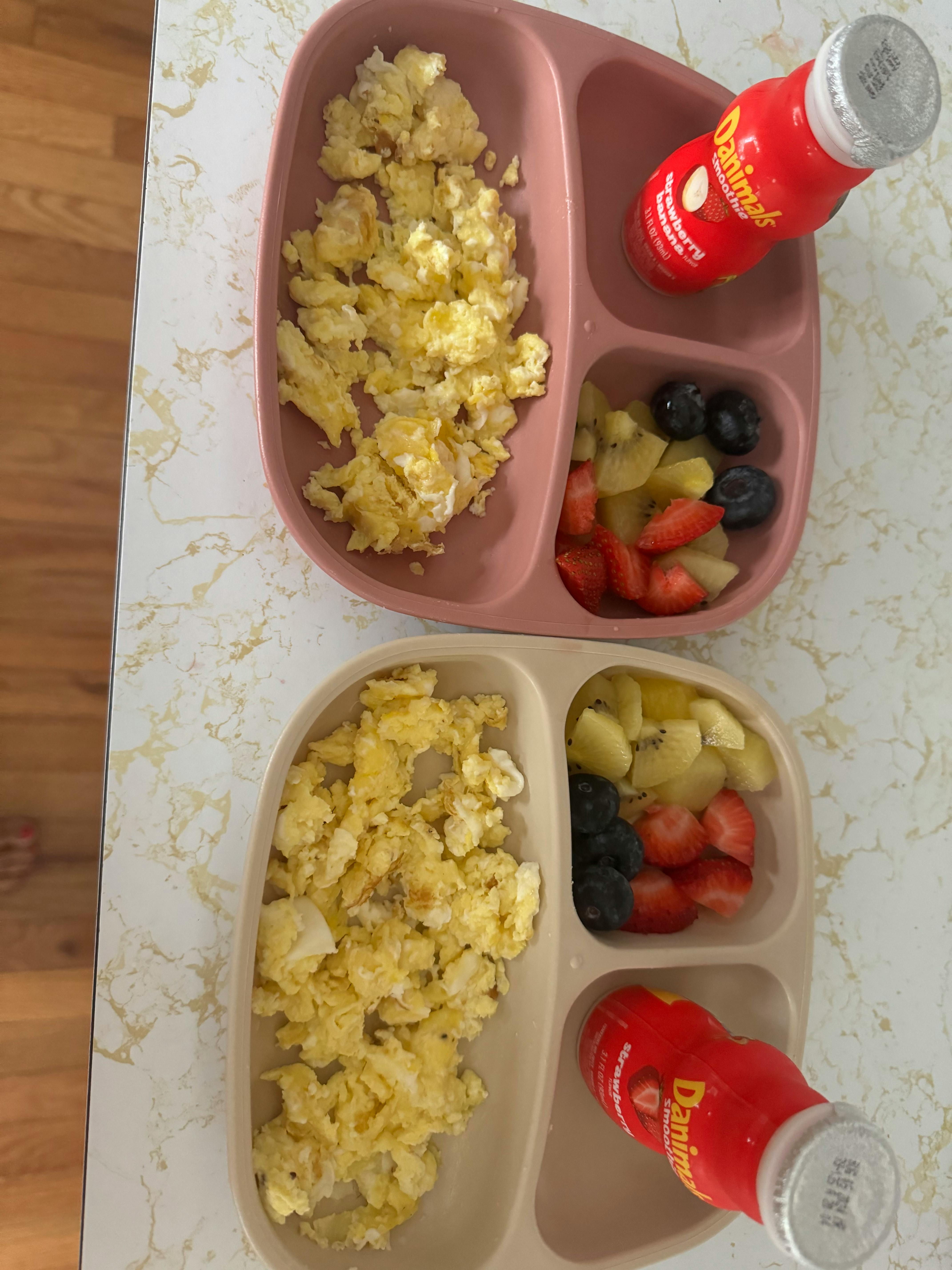 Two plates of scrambled eggs, fruit, and yogurt drinks