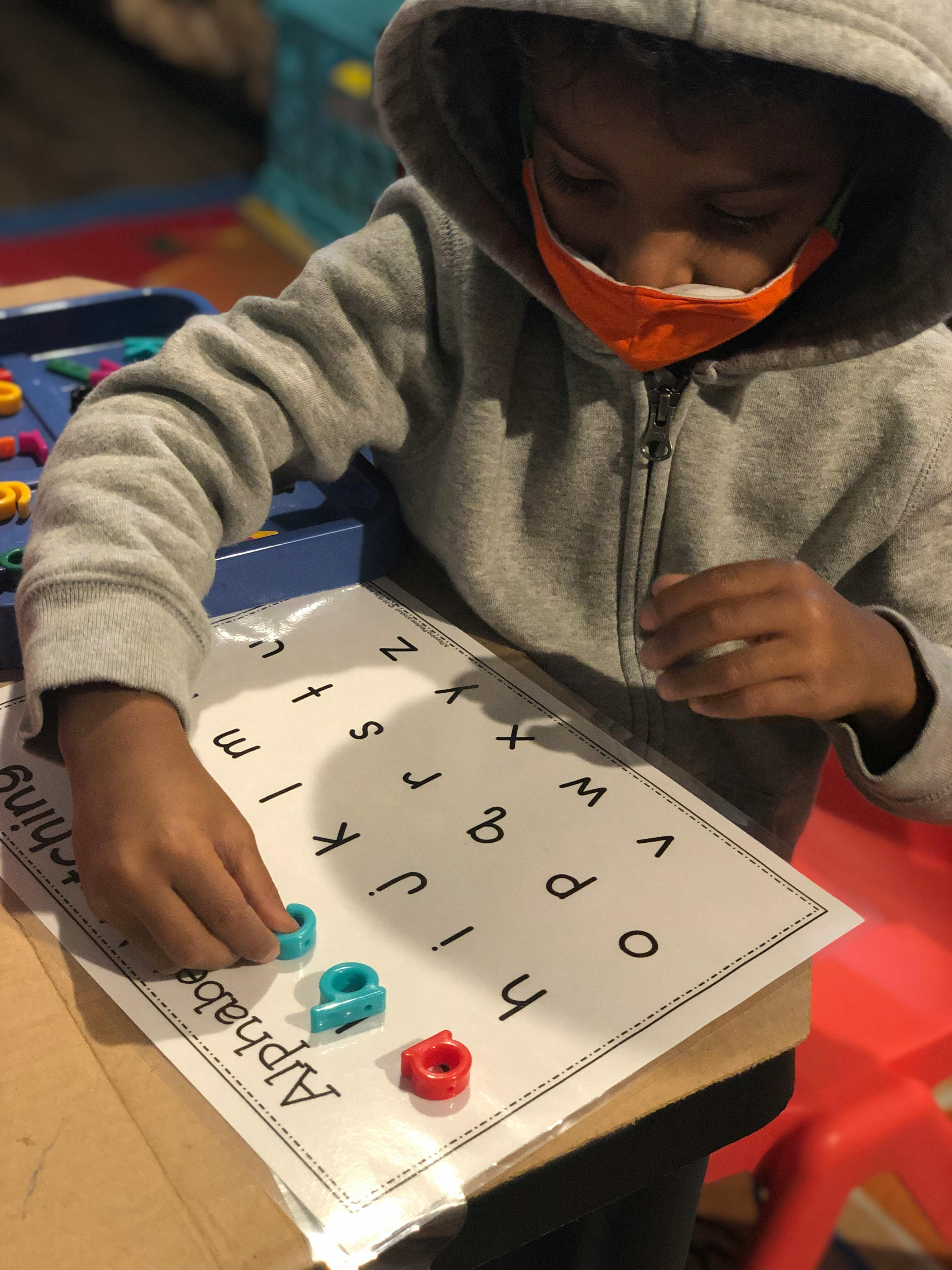 Child in a mask placing letter pieces on an alphabet sheet