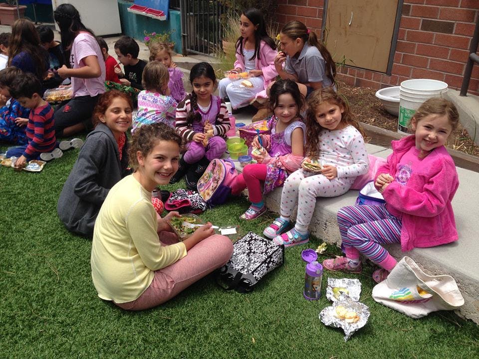 Group of children sitting on grass and concrete, some eating