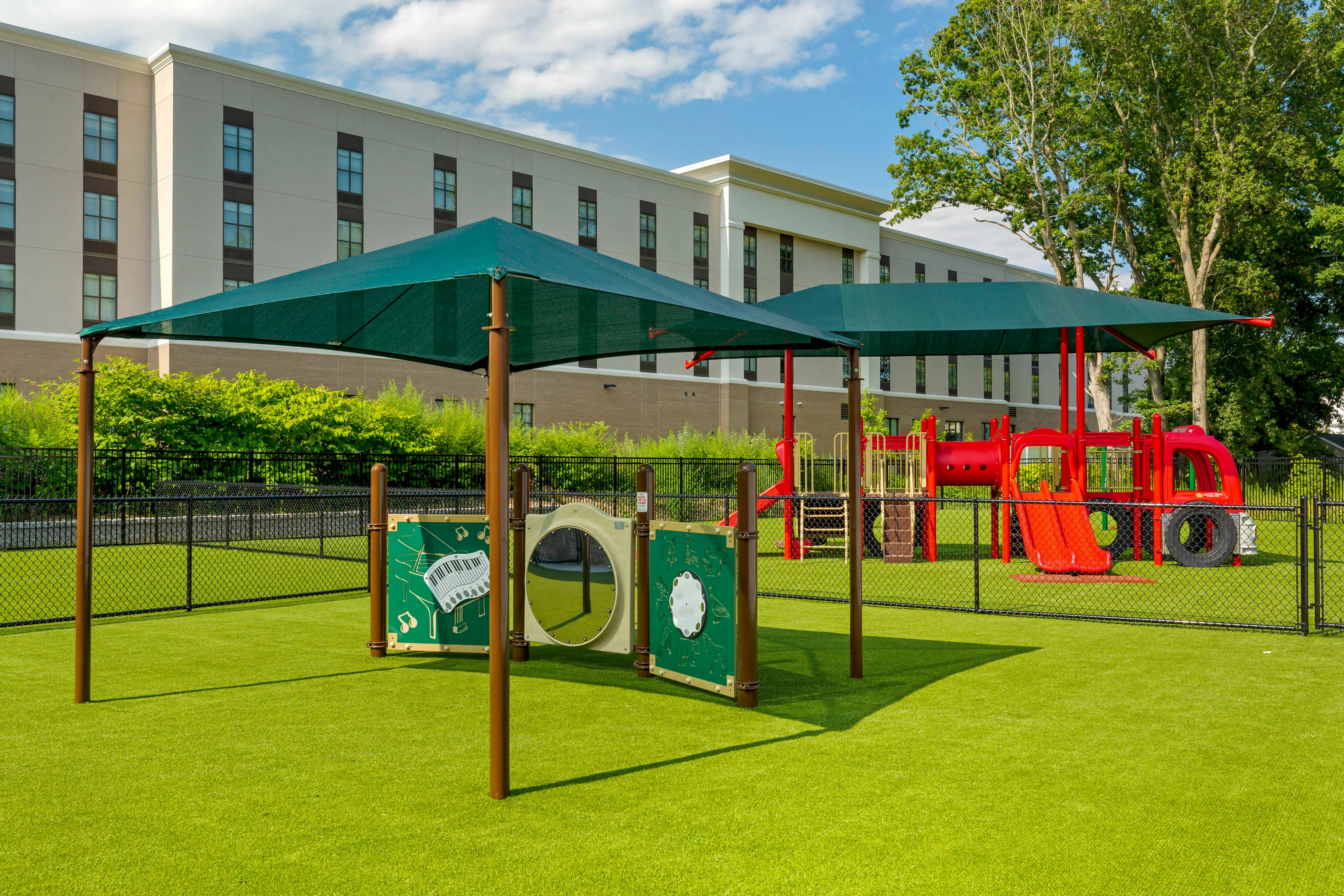 Playground with green turf, red slides, and a climbing structure under green shade canopies