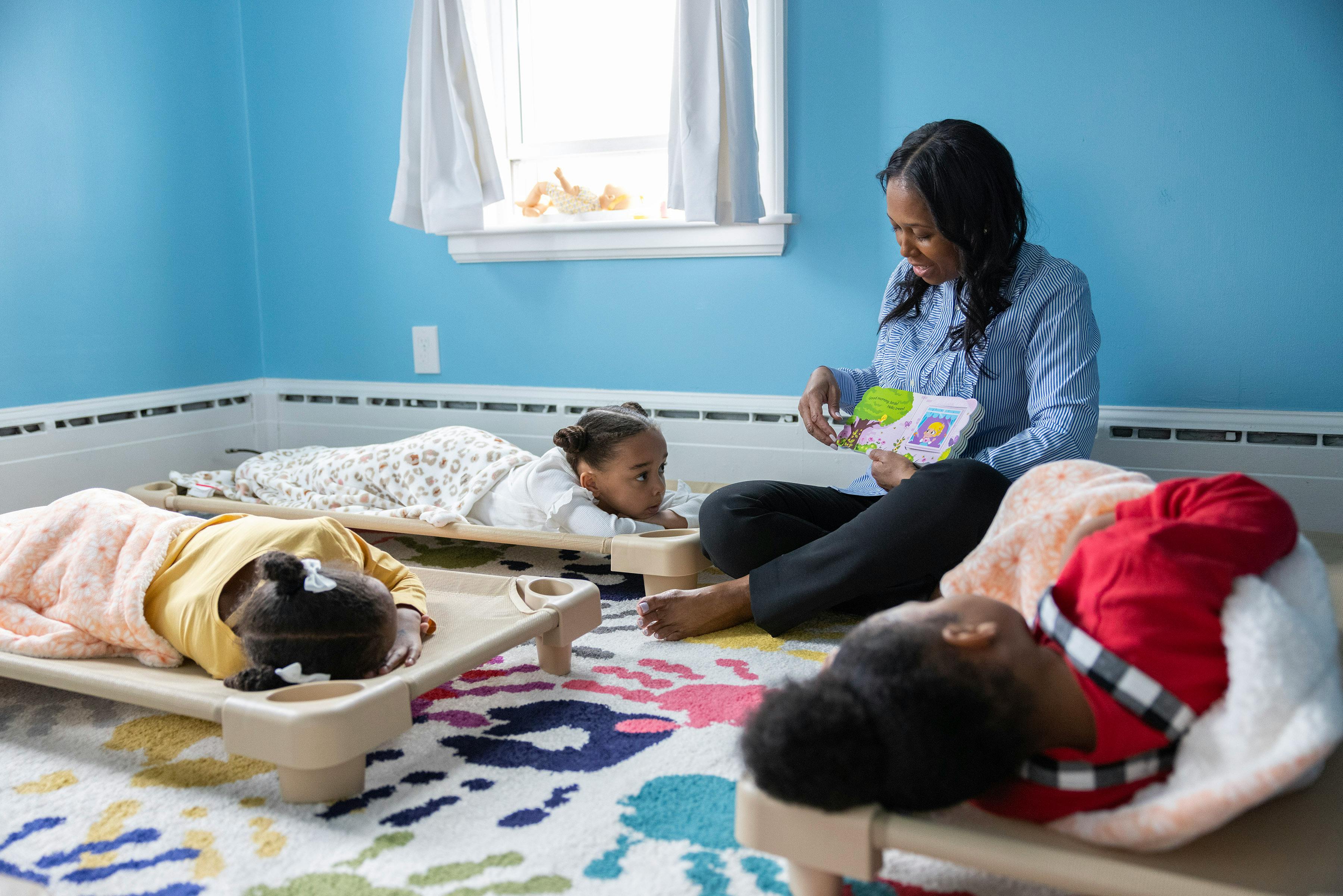 Person reading to children resting on cots in a room