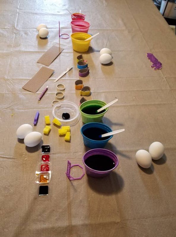 Eggs and cups of dye on a table covered with plastic
